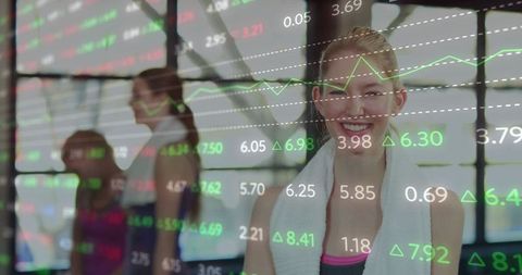 Smiling woman posing in gym with stock market data overlay and fitness group behind