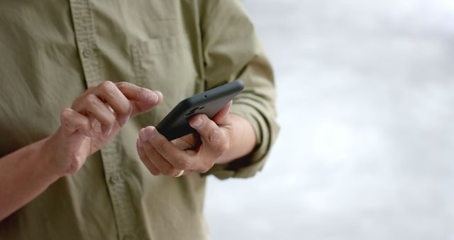 Close-up of person using smartphone for messaging or browsing, dressed in casual outfit. Useful for technology, communication, and lifestyle themes.