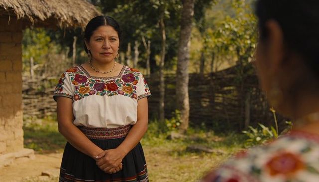 Standing woman wearing embroidered blouse and woven belt in rural village yard