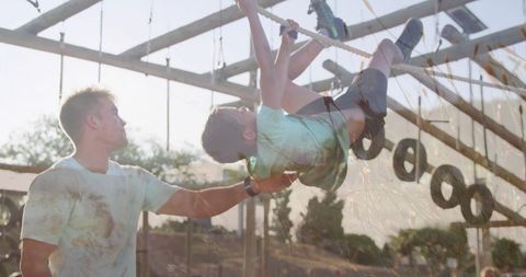 Boy climbing rope on outdoor obstacle course with adult assistance