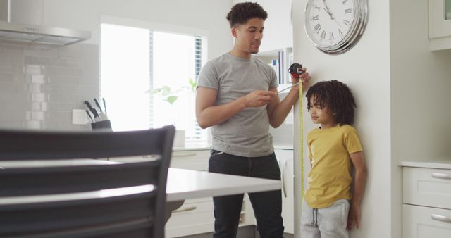 Happy biracial man and his son measure height in kitchen. domestic life, spending time at home.