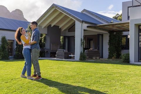 Young couple embracing on lush lawn in front of modern house with patio and mountain view