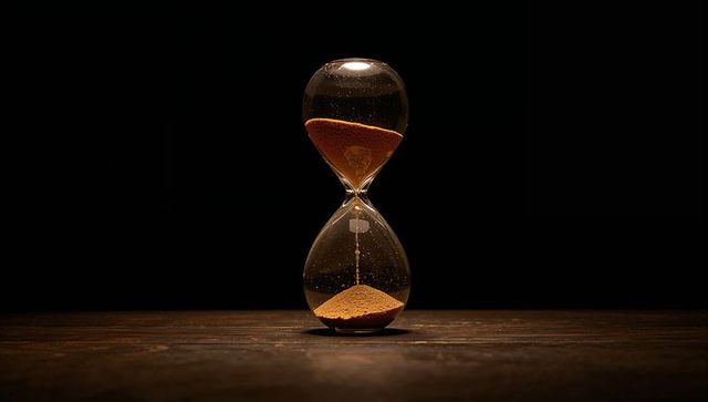 Moody hourglass pouring amber sand on dark wood surface with dramatic spotlight
