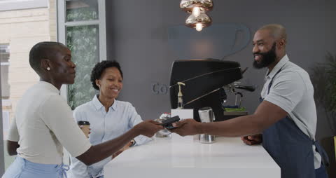 Smiling Barista Assisting Customers with Contactless Payment in Cafe