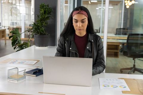 Young professional woman working on laptop in modern office reviewing analytics charts and reports