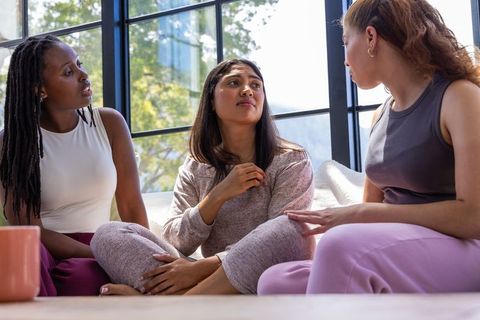 Three women sharing emotional support during casual living room conversation