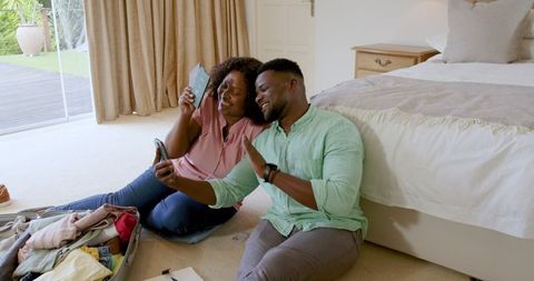 Smiling Couple Taking Selfie While Packing for Vacation