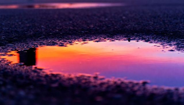 Vivid sunset reflection on asphalt puddle showing colorful gradient and soft bokeh
