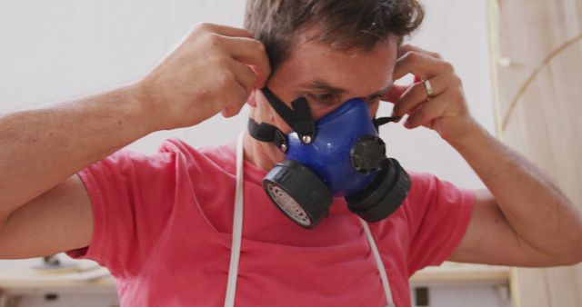 Man adjusting a blue protective mask, suitable for illustrating concepts of workplace safety, health protection, industrial work, or personal protective equipment. Good use for safety training materials, occupational health articles, and industrial equipment promotions.