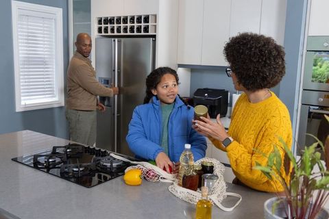 Multiracial family organizing groceries at kitchen island with child and mother holding jar