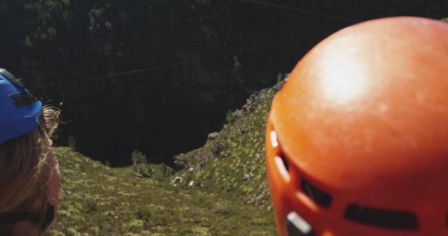 Adventurers wearing safety helmets looking at a rocky cliffside, suggesting a climbing or rappelling activity. Suitable for use in outdoor adventure promotions, climbing or extreme sports advertisements, and safety gear marketing campaigns.