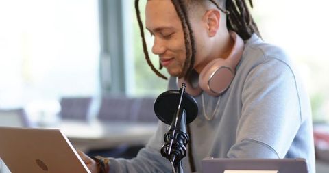 African american man podcasting and editing on laptop with mic and headphones at home