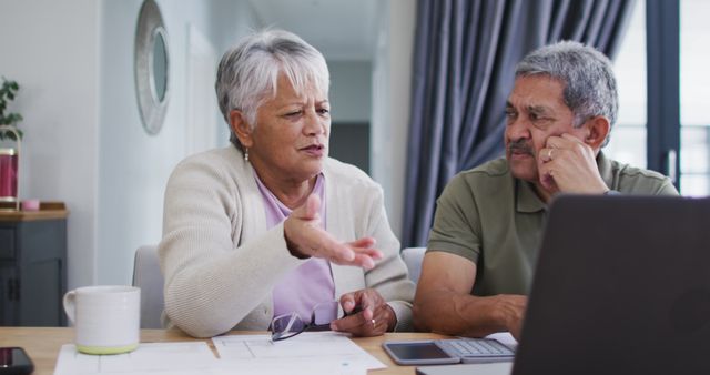 Senior couple having serious discussion while using laptop for financial planning at home. Ideal for websites and articles about retirement planning, financial management, elderly lifestyle, and family budgeting discussions. Visually represent home office environment, mature relationship communication, and thoughtful decision-making processes.