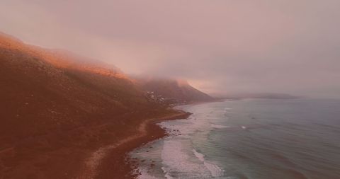 Misty Coastal View with Ocean Waves and Mountains at Sunset