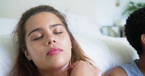 Diverse friends reclining with rose quartz facial roller practicing self-care at home