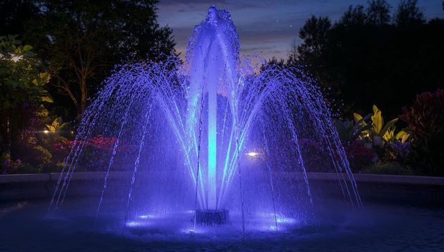 Blue-purple illuminated fountain at dusk in garden with symmetrical multi-jet water display