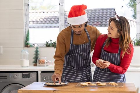 Couple baking christmas cookies at kitchen island wearing santa hat and reindeer antlers