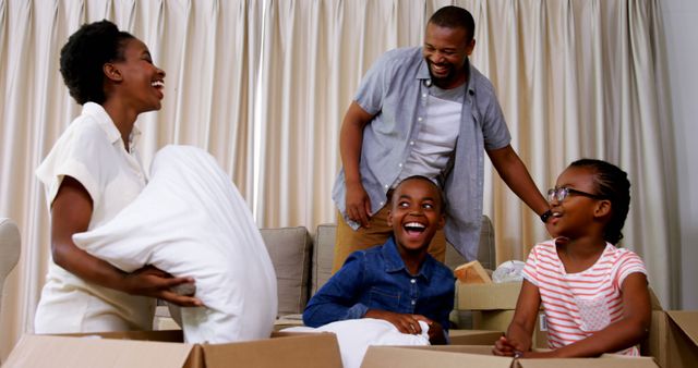 A joyful African American family is engaged in a playful pillow fight, with copy space. Smiles and laughter fill the room as they create memories during a break from unpacking moving boxes.