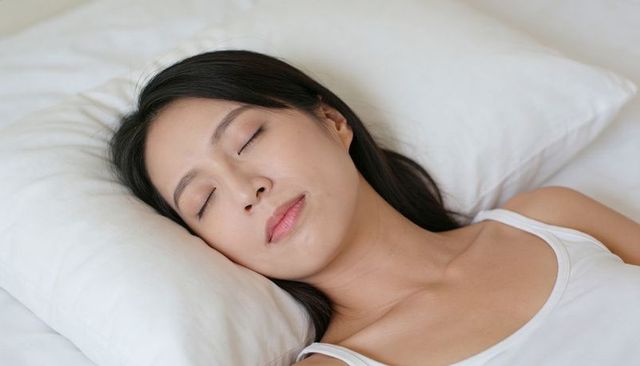 Asian woman sleeping peacefully on white pillow in minimalist bedroom