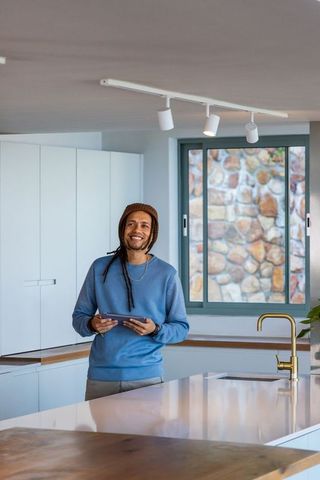 African american man smiling holding tablet in modern minimalist kitchen with brass faucet