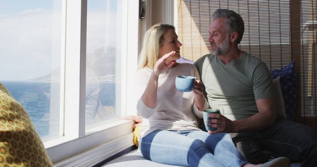 Relaxing caucasian mature couple drinking coffee and talking in sunny living room. enjoying leisure time at home