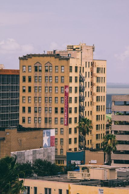 Yellow office buildings in a mid-size city with juxtaposition of other structures including palm trees and view of the sea in the background. Suitable for urban architecture, downtown life, business hub, and real estate use cases.