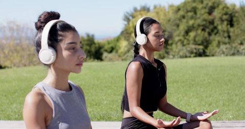 Women meditating outdoors with headphones in serenity
