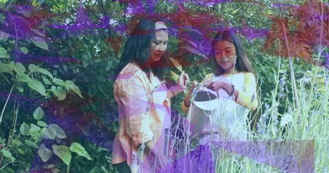 Two Women Watering Backyard Garden Inspecting Plants with White Watering Can