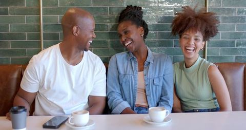 Laughing friends enjoying coffee and conversation in cafe booth lifestyle portrait