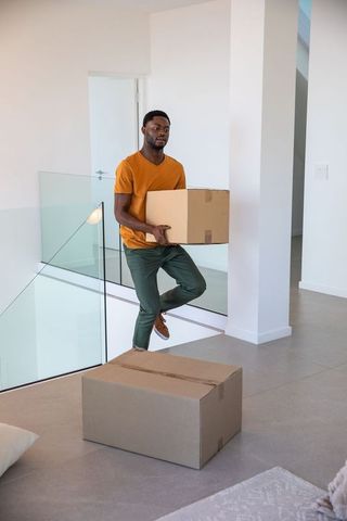 Man carrying moving box in modern interior with glass railing