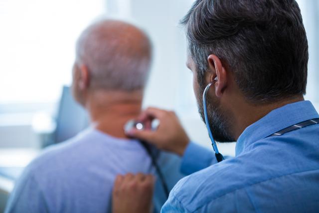 Male doctor using stethoscope to examine elderly patient in hospital. Ideal for healthcare, medical services, senior care, and doctor-patient relationship concepts.