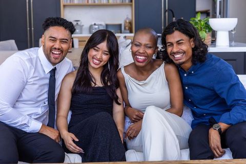 Diverse friends laughing and leaning on sofa wearing formal attire in modern living room