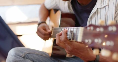 Guitarist playing acoustic guitar on lap in warm window light closeup with bokeh, fretboard focus