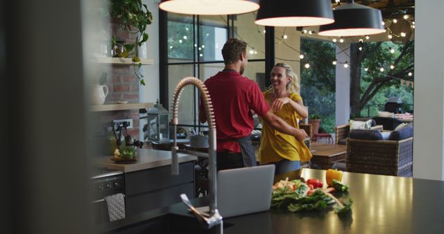 Happy caucasian couple having fun dancing together while preparing meal in kitchen. Romance, fun, domestic life and togetherness.