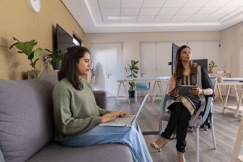 Asian women collaborating in modern lounge using laptop and tablet