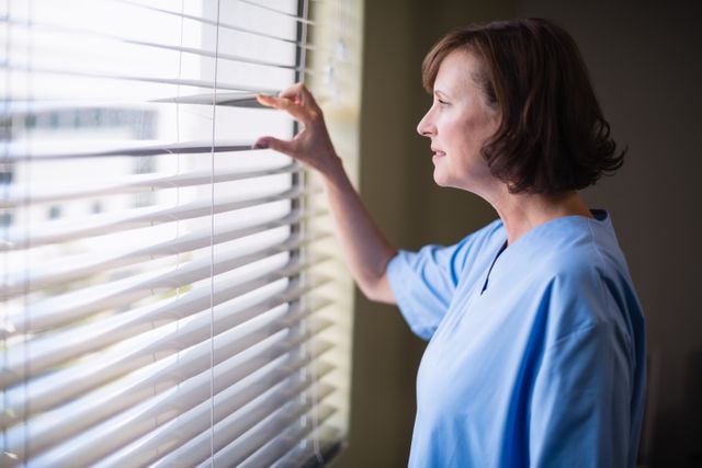 Thoughtful nurse looking out through window in hospital