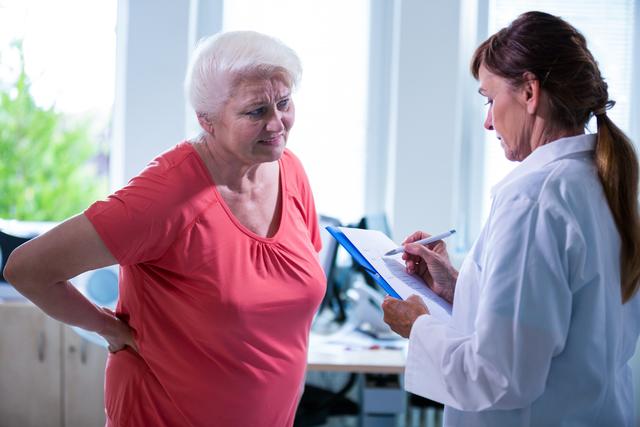 Senior woman consulting a doctor about back pain in a hospital setting. Useful for healthcare, medical advice, elderly care, and patient-doctor interaction themes.