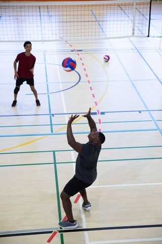 Diverse male players practicing volleyball serving and setting on indoor gym court team drill
