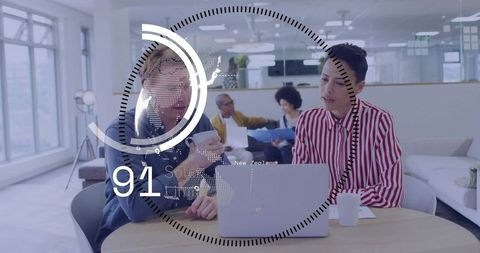 Collaborating team working on laptop in modern coworking space with data overlay