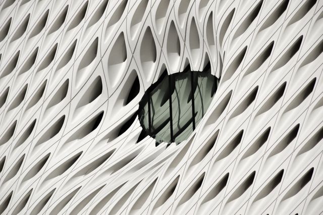 This photo showcases a modern architectural building with a unique window design. The facade features an abstract geometric pattern with white and irregular shapes, creating a striking visual effect. This image can be used for design, architecture, and urban development projects, or for showcasing innovative contemporary buildings.