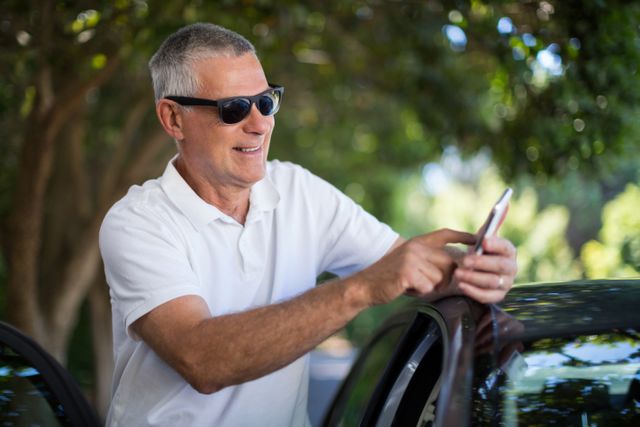 Smiling senior man using smart phone while standing by car