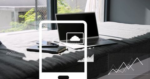 Placing laptop on bed in sunlit minimal workspace with smartphone, notebook and charts