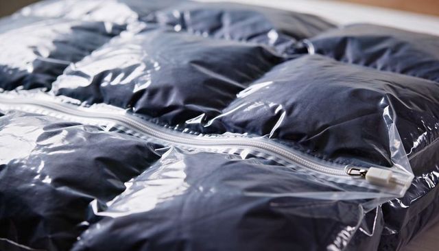 Compressing dark duvet in clear vacuum storage bag with white slider zipper