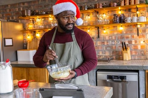 African american man whisking batter in santa hat and apron in cozy festive kitchen
