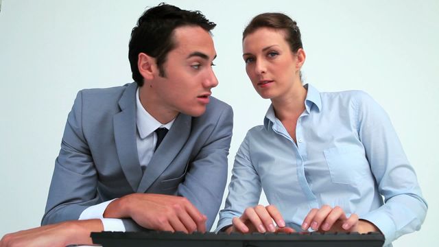 Businessman and businesswoman engaged in focused work on computer. Useful for depicting collaboration, office teamwork, professional activities, corporate environments, cooperative work, and communication within a business setting.