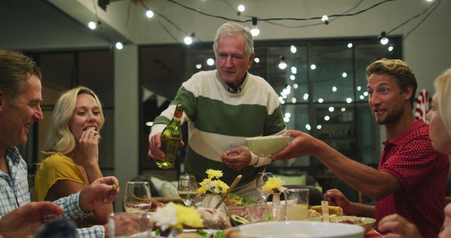 Family sharing meal outdoors under string lights during summer evening. Elderly man pouring drink while others pass bowls and enjoy food. Great for themes on family bonding, casual dining, festive occasions, and intergenerational connections.