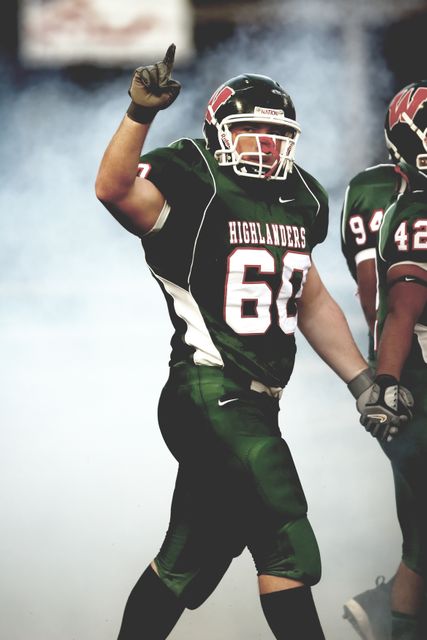 Football player wearing uniform celebrating a touchdown during a game on the field. Suitable for use in sports articles, football blogs, team branding, and athletic success stories.