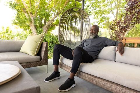 Senior african american man relaxing on rattan patio sofa near hanging egg chair in garden