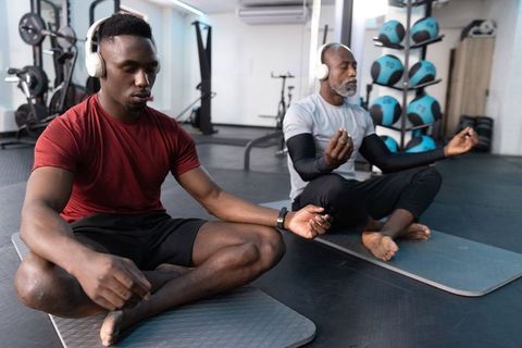 Younger and senior african american men meditating on mats in gym wearing headphones
