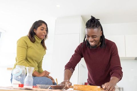 African american man and asian woman baking together in modern kitchen, rolling dough